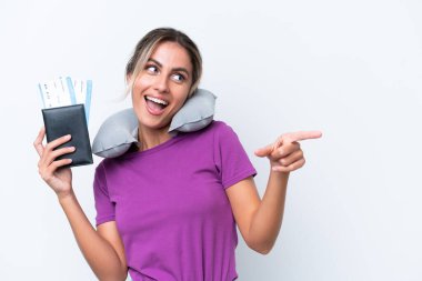 Şişirilebilir Seyahat Yastığı ile genç, güzel Uruguaylı kadın beyaz arka planda izole edilmiş bir şekilde parmak ucunda bir ürün sunuyor.