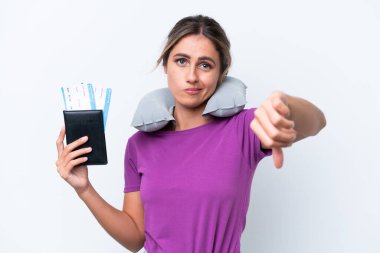 Şişirilebilir Seyahat Yastığı olan genç, güzel Uruguaylı kadın beyaz arka planda izole edilmiş, olumsuz ifadeli baş parmağını gösteriyor.