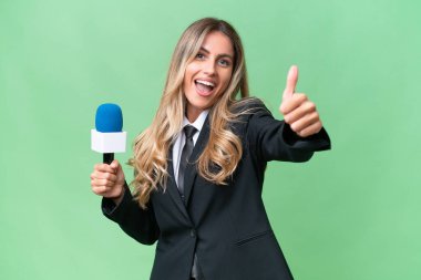 Genç, güzel Uruguaylı bir televizyon sunucusu, izole edilmiş bir arka planda, başparmakları havada, çünkü iyi bir şey oldu.