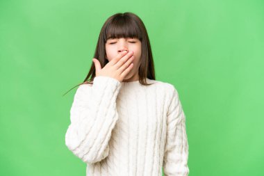 Küçük beyaz kız izole edilmiş arka planda esniyor ve geniş ağzı eliyle kapatıyor.