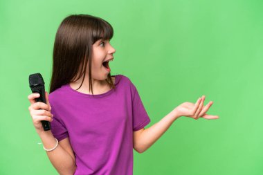 Küçük şarkıcı kız, izole edilmiş bir arka planda sürpriz bir yüz ifadesiyle mikrofonu eline aldı.