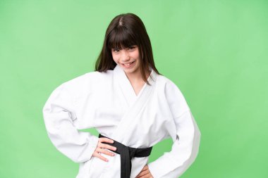 Küçük beyaz kız izole edilmiş arka planda karate yapıyor. Kolları kalçasında ve gülümsüyor.