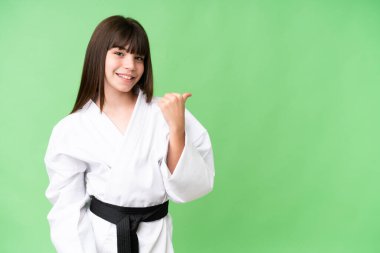 Küçük beyaz kız karate yapıyor izole edilmiş arka planda bir ürünü sunmak için kenarı işaret ediyor.