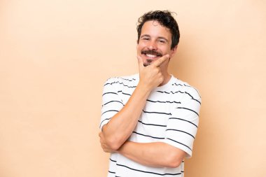 Young caucasian man isolated on beige background happy and smiling