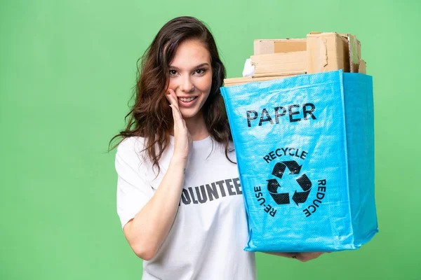 年轻的高加索女人拿着一个装满纸的回收袋 在孤立的背景下回收 低声说着什么 — 图库照片