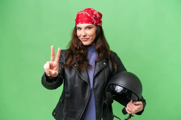 若いですCaucasian女性とともにオートバイヘルメット上の隔離された背景笑顔とショー勝利サイン — ストック写真