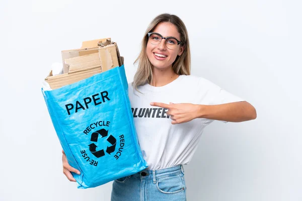 若いかなりウルグアイの女性は白いクロマの背景に隔離されたリサイクルするために紙でいっぱいのリサイクルバッグを保持し それを指す — ストック写真
