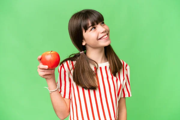 Stock image Little caucasian girl holding an apple over isolated background looking up while smiling