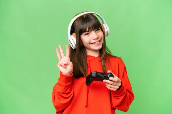 一个小高加索女孩快乐地和一个视频游戏控制器一起玩在一个孤立的背景下 用手指数着三个 — 图库照片