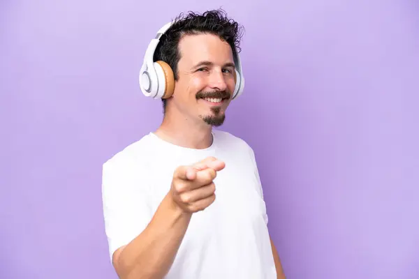 Young Caucasian Man Isolated Purple Background Listening Music Pointing Front — Stock Photo, Image