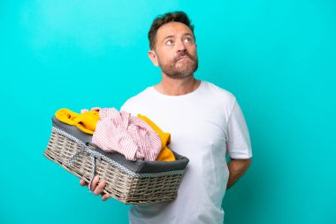 Elinde çamaşır sepeti olan orta yaşlı bir kadın mavi arka planda izole edilmiş bir şekilde yukarı bakıyor.