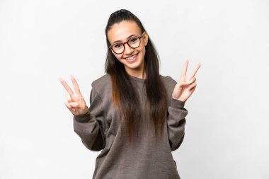 İzole edilmiş beyaz arka planda genç bir Arap kadın iki eliyle zafer işareti gösteriyor.