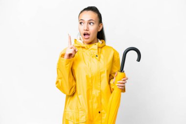Yağmura dayanıklı ceketi ve şemsiyesi olan genç bir Arap kadın izole edilmiş beyaz arka planda parmağını kaldıran bir fikir düşünüyor.