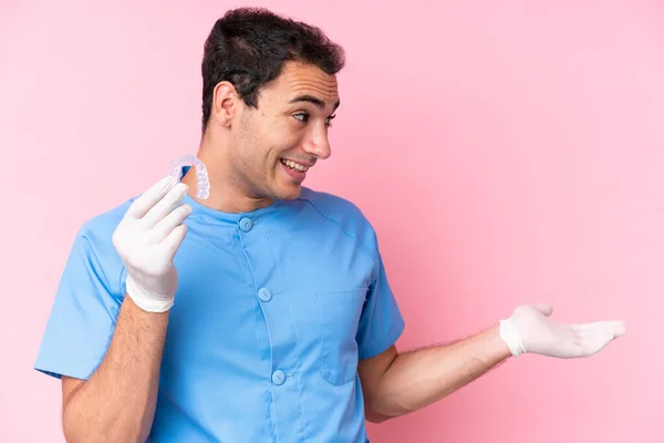 Dentist caucasian man holding invisible braces isolated on pink background with surprise expression while looking side
