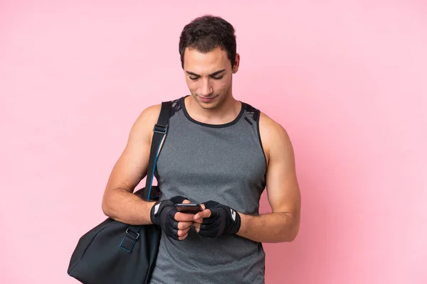 年轻的体育高加索人 背负着粉色背景的运动包 用手机传达着一个信息 — 图库照片