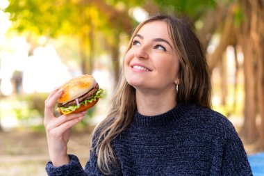 Genç, güzel Romen kadın elinde hamburgerle gülümseyerek yukarı bakıyor.