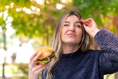 Genç, güzel Romen kadın elinde hamburgerle kuşkuları ve kafa karıştırıcı bir ifadeyle