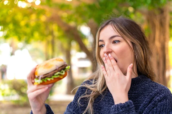 Młoda Ładna Rumuńska Kobieta Trzyma Hamburgera Świeżym Powietrzu Zaskoczeniem Wstrząśnięty — Zdjęcie stockowe