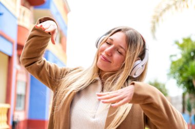 Açık havada müzik dinleyen ve dans eden güzel sarışın bir kadın.