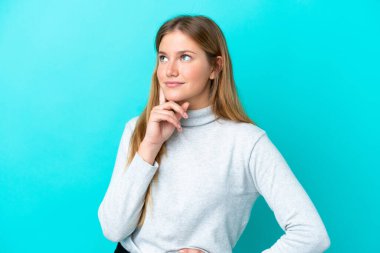 Mavi arka planda izole edilmiş genç sarışın kadın yukarı bakarken bir fikir düşünüyor.