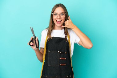 Genç Litvanyalı terzi kadın mavi arka planda izole edilmiş, telefon jesti yapıyor. Bana geri dönüş işareti ver.