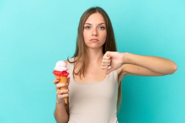 Kornet dondurmalı genç Litvanyalı kadın mavi arka planda izole edilmiş, olumsuz ifadeli baş parmağını gösteriyor.