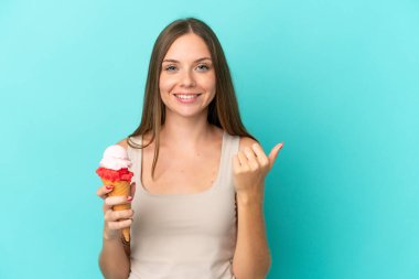 Young Lithuanian woman with cornet ice cream isolated on blue background pointing to the side to present a product