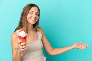 Kornet dondurmalı genç Litvanyalı kadın, mavi arka planda izole edilmiş. Davet etmek için ellerini yana uzatıyor.