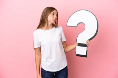 Genç Litvanyalı bir kadın pembe arka planda izole edilmiş elinde bir soru işareti simgesi ve üzgün bir ifadeyle