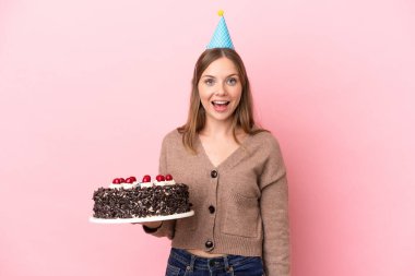 Elinde doğum günü pastası tutan Litvanyalı genç bir kadın. Pembe arka planda, şaşırmış bir yüz ifadesi var.