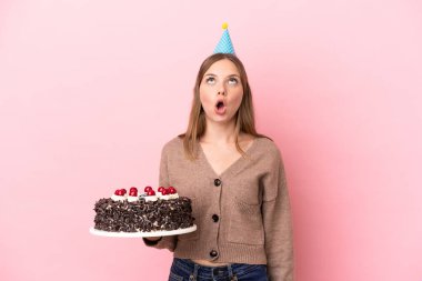 Elinde doğum günü pastası tutan Litvanyalı genç bir kadın pembe arka planda izole edilmiş yukarı bakıyor ve şaşırmış bir ifadeyle