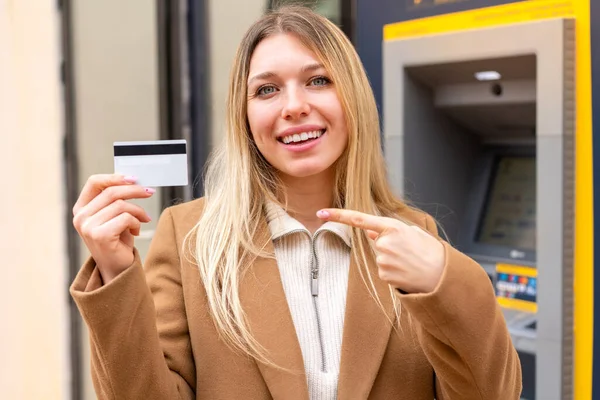 Młoda Ładna Blondynka Trzymająca Kartę Kredytową Zewnątrz Wskazująca — Zdjęcie stockowe