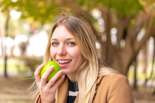 年轻漂亮的金发女人在户外拿着一个苹果 — 图库照片