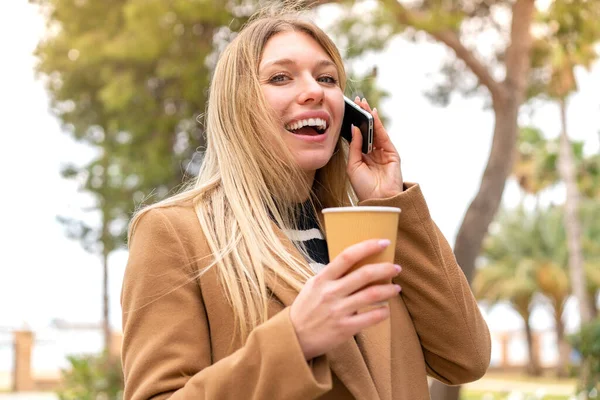 Mladý Pěkný Blondýnka Žena Pomocí Mobilního Telefonu Drží Odnést Kávu — Stock fotografie