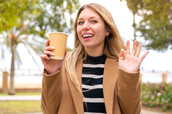 Mladý Pěkný Blondýnka Žena Drží Odnést Kávu Venkovním Salutování Rukou — Stock fotografie