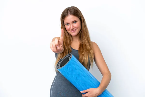 年轻的女运动员一边去上瑜伽课 一边拿着垫子展示和举起一只手指头 — 图库照片