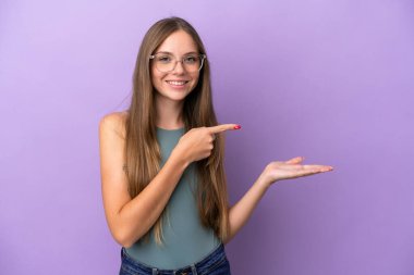 Mor arka planda izole edilmiş genç Litvanyalı kadın bir ilan vermek için avucunun içinde hayali bir kopyalama alanı tutuyor.