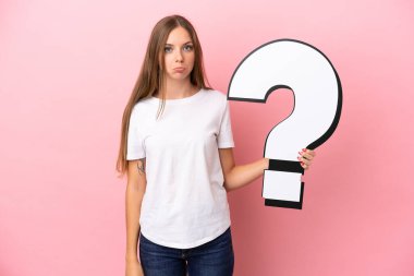 Genç Litvanyalı bir kadın pembe arka planda izole edilmiş elinde bir soru işareti simgesi ve üzgün bir ifadeyle