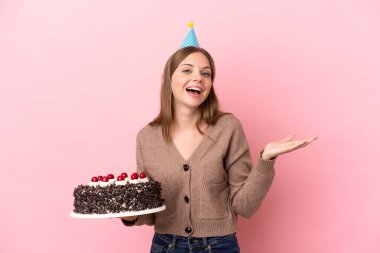 Elinde doğum günü pastası tutan Litvanyalı genç kadın pembe arka planda şok olmuş yüz ifadesiyle izole edilmiş.