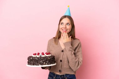 Elinde doğum günü pastası tutan genç Litvanyalı kadın pembe arka planda izole edilmiş gülümserken yukarı bakıyor.