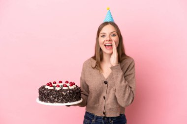 Elinde doğum günü pastası tutan Litvanyalı genç bir kadın pembe arka planda ağzı açık bağırıyor.