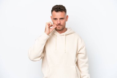 Beyaz arka planda izole edilmiş beyaz tenli yakışıklı genç bir adam sessizlik işareti gösteriyor.