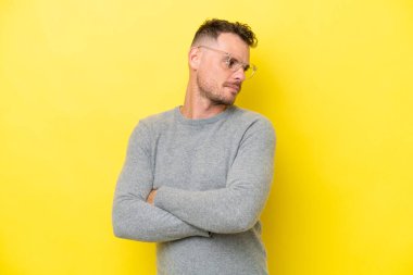 Sarı arka planda izole edilmiş beyaz, yakışıklı genç bir adam kollarını kavuşturuyor.