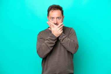 Middle age caucasian man isolated on blue background covering mouth with hands