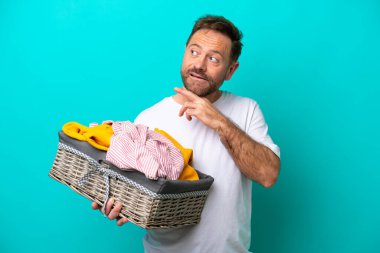 Mavi arka planda izole edilmiş çamaşır sepetini tutan orta yaşlı bir kadın gülümserken yukarı bakıyor.