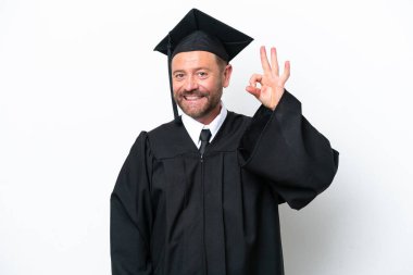 Orta yaşlı üniversite mezunu beyaz arka planda izole edilmiş parmaklarıyla tamam işareti gösteriyor.