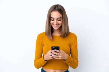 Beyaz arka planda izole edilmiş genç beyaz kadın cep telefonuyla mesaj ya da e-posta gönderiyor.