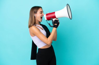 Young sport woman isolated on blue background shouting through a megaphone