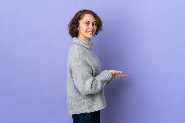 Young English woman isolated on purple background extending hands to the side for inviting to come