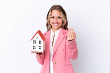 Rus emlakçı, beyaz arka planda izole edilmiş bir oyuncak evi tutuyor ve para hareketi yapıyor.